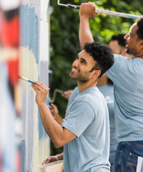 A cheerful group of men donate their time and talents to repaint walls covered in graffiti at the local park.