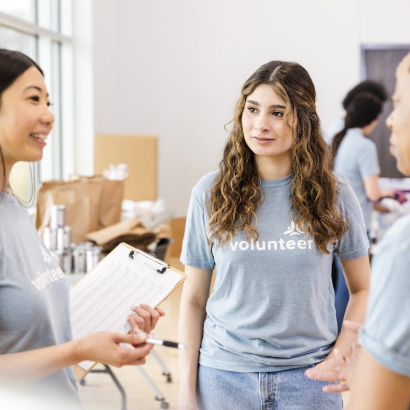 Three diverse young women working together, casual attire, clipboard, teamwork, charity.
